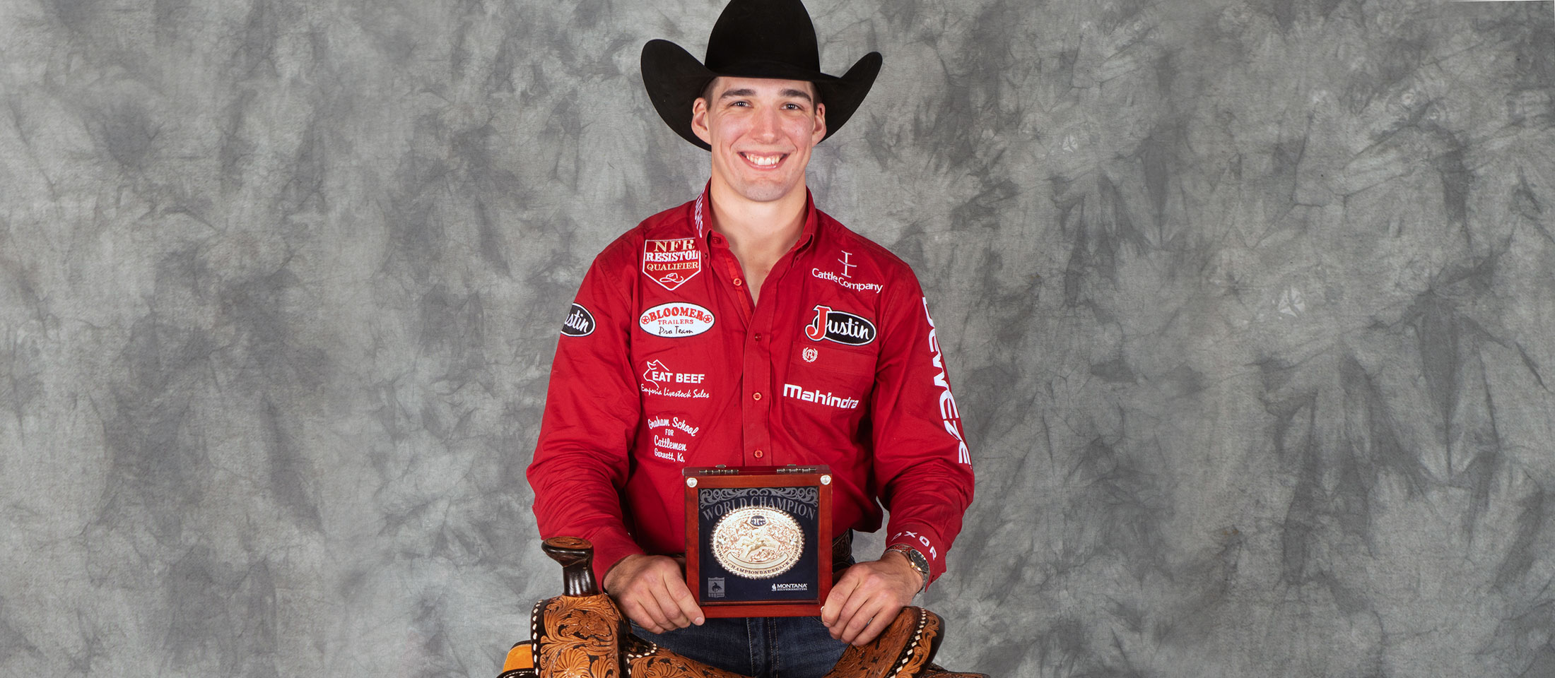 Jess Pope posing and standing behind his world champion saddle and holding his gold buckle